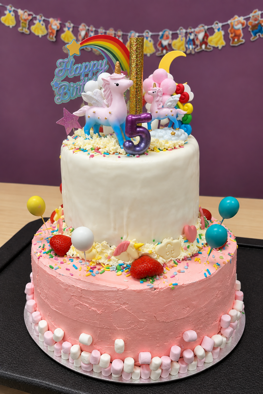 Two-tier pink and white birthday cake with unicorn figures and marshmallows