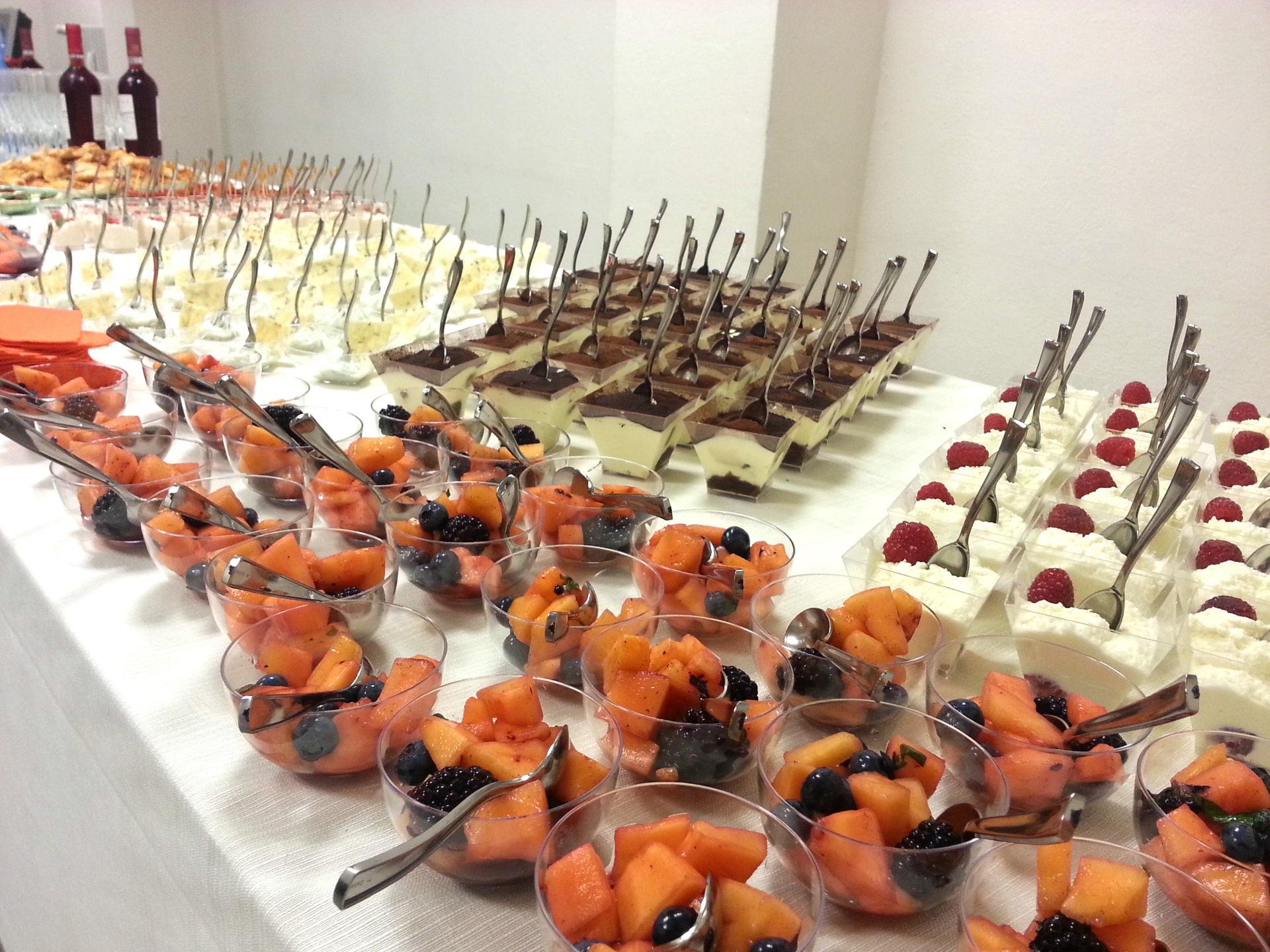 Long buffet table with fruit cups, tiramisù and small desserts