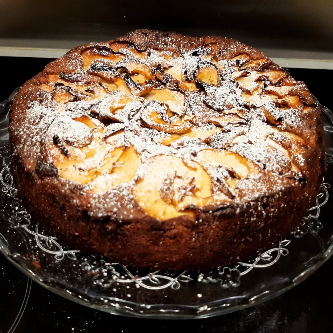 Apple cake dusted with icing sugar on a glass cake stand