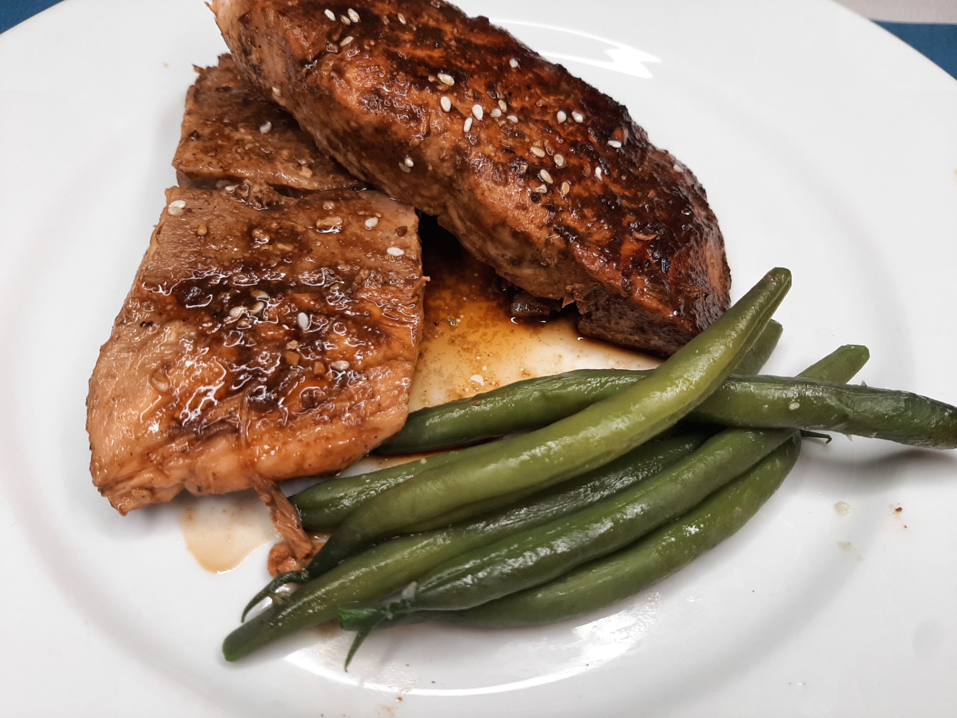 Miso-glazed salmon with sesame seeds and green beans on a white plate
