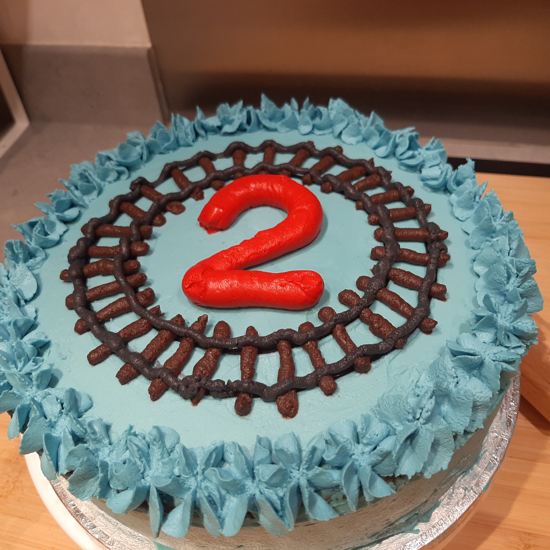 Blue round birthday cake with chocolate railway tracks and a red number 2