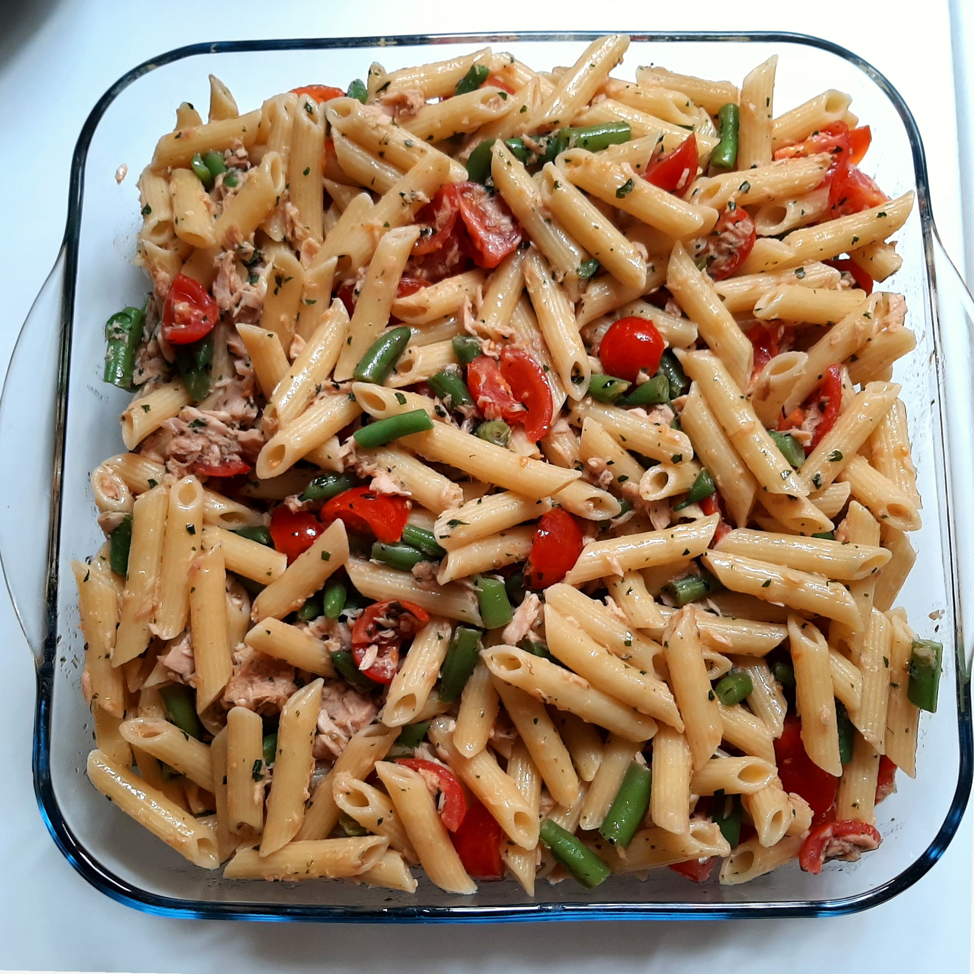 Penne pasta with tuna, cherry tomatoes and green beans in a glass dish