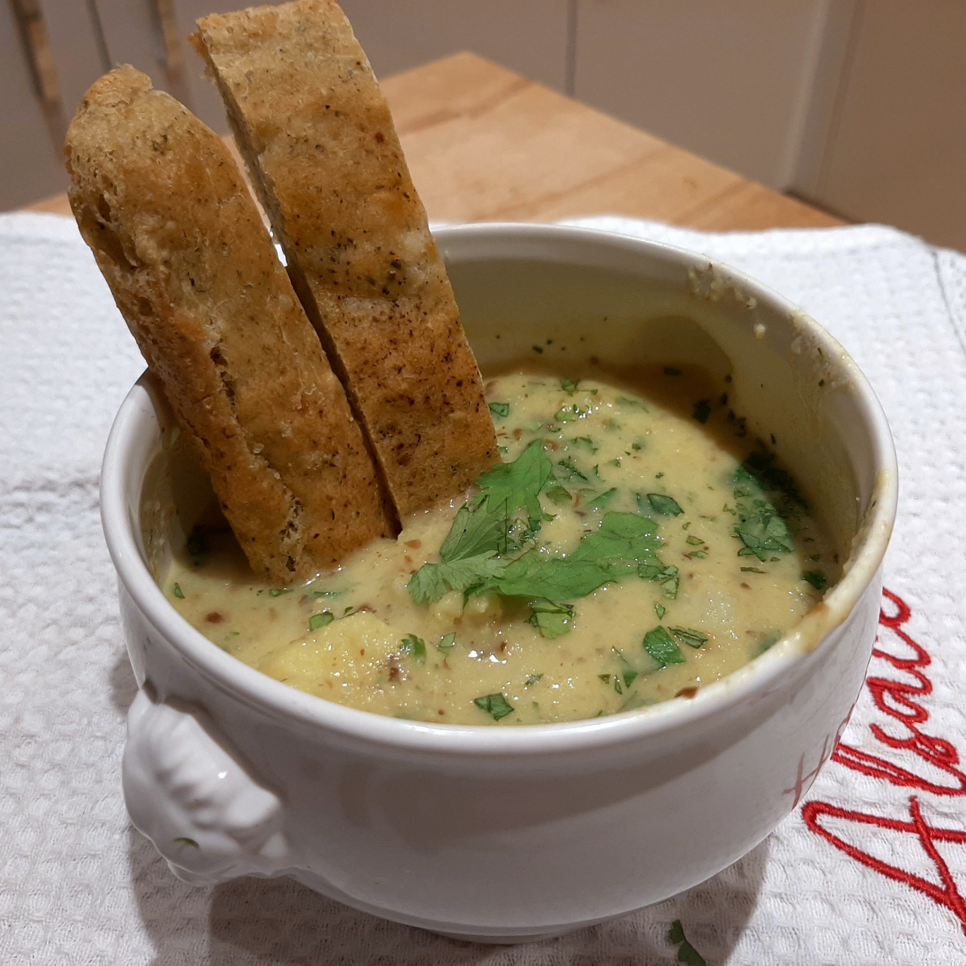 Leek soup served in a white lion-head bowl with crusty bread on an Alsatian cloth